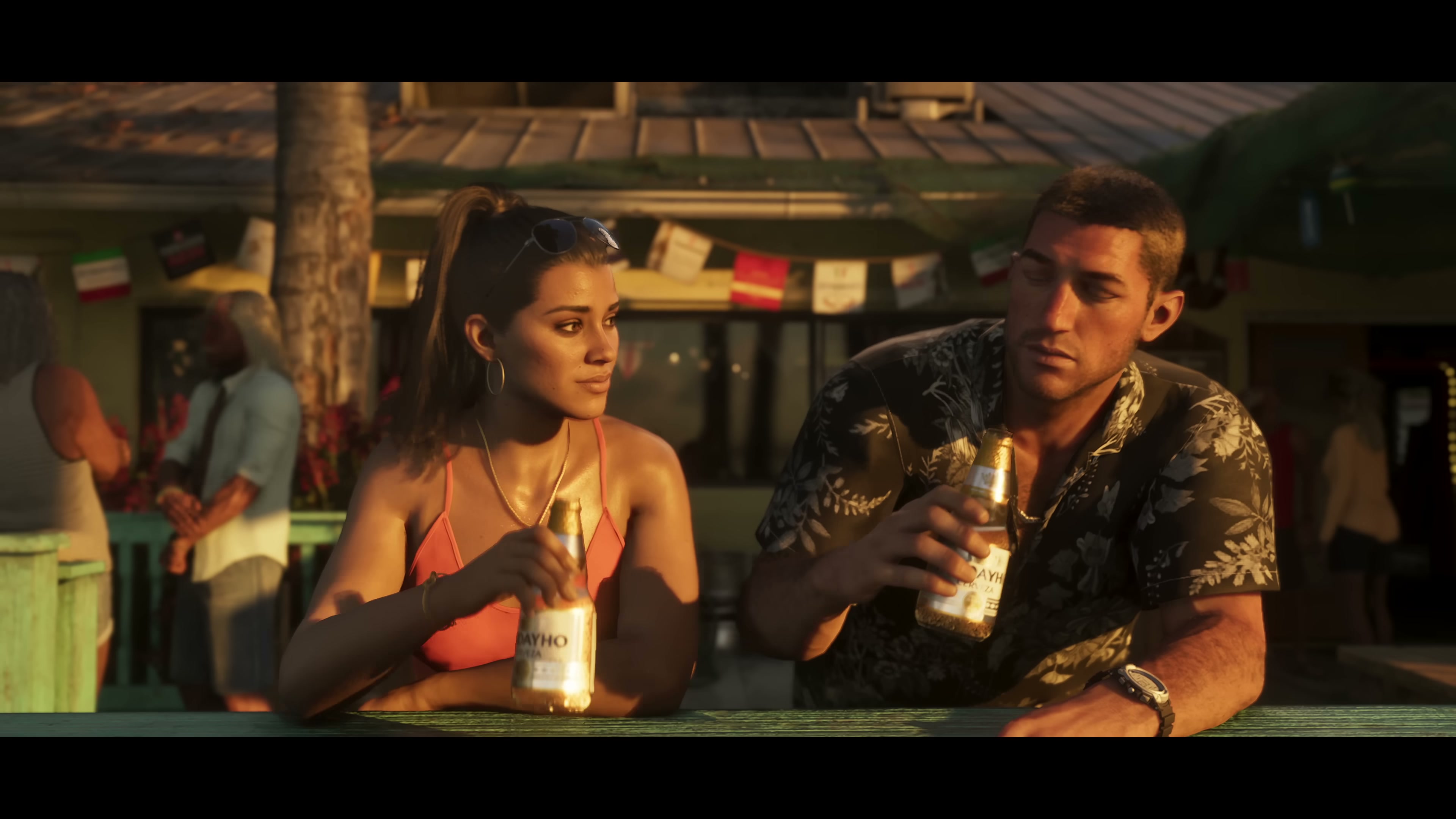 Jason and Lucia sit at an outdoor beachside bar at sunset, each holding a bottle of beer.
